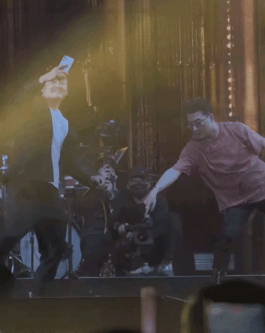 汪峰正在台上准备开口唱歌，一位男粉丝突然举着手机冲上来，要求合影，完全没有注意到