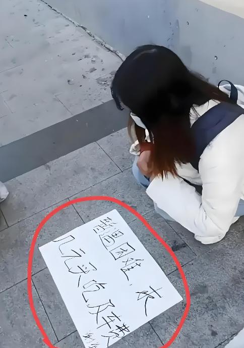 小姐姐蹲路边举白纸求助，写着偶遇困难，只求几块钱买饭和车费。 一身干净外套，背着