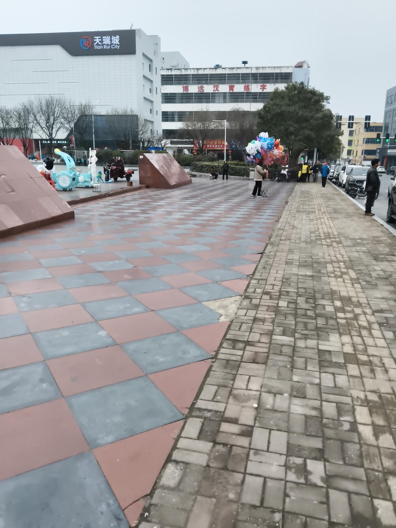 远处，“天瑞城”的招牌在灰蒙天色下格外醒目，旁边的楼宇静静伫立。广场上，卖气球的