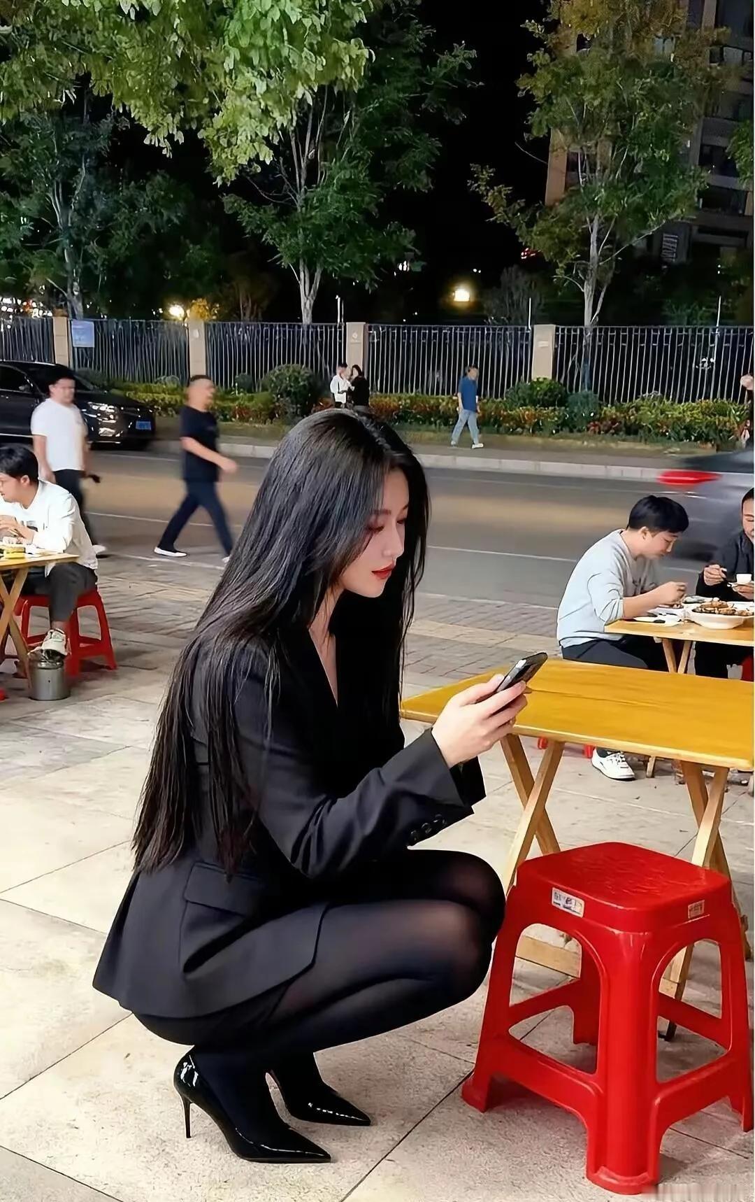 夜晚街边，优雅黑衣女子低头看手机，静谧氛围中尽显都市风情。