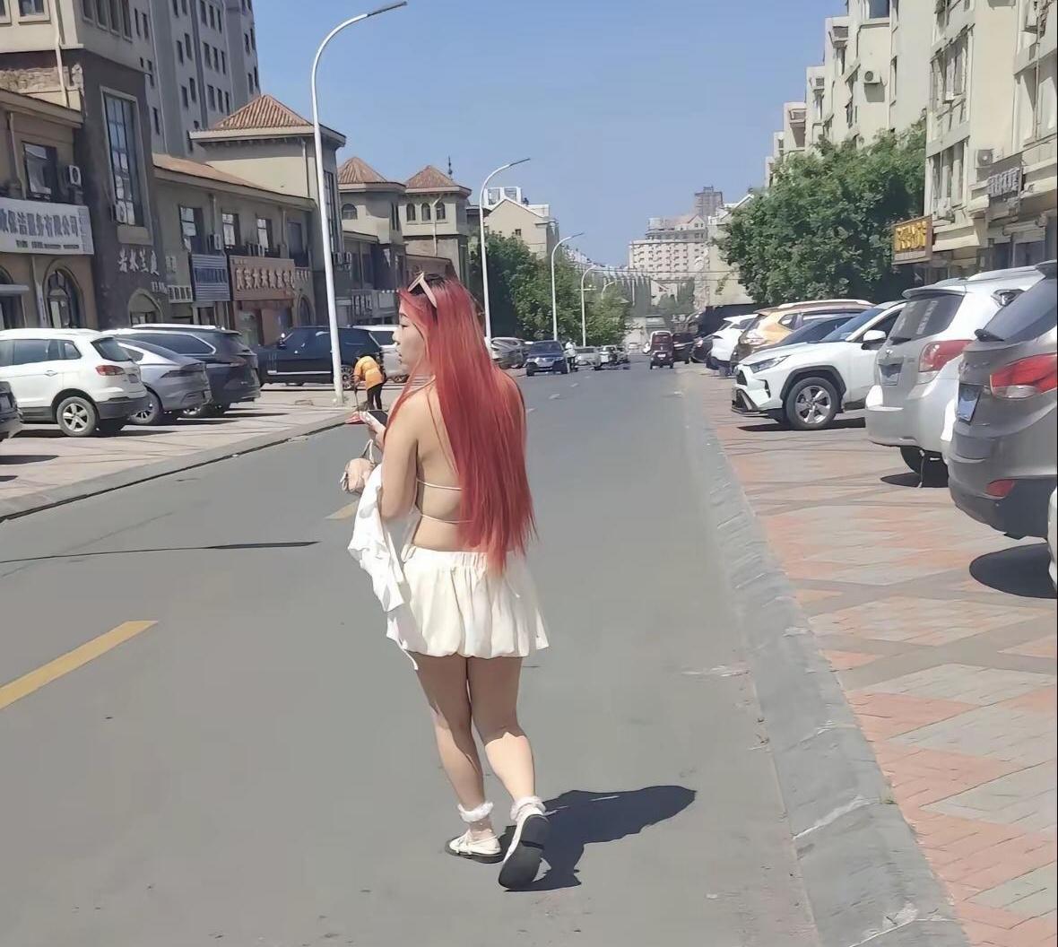 姑娘，今天有这么热吗？看你红发飘扬、露背装清凉，连外套都拎在手里，这架势，再热也