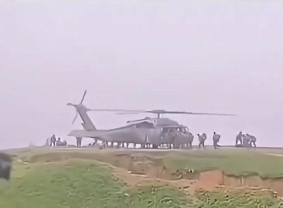 草坡之上，军用直升机稳稳悬停，旋翼搅动起漫天烟尘。士兵们快速登机、集结，身影在灰