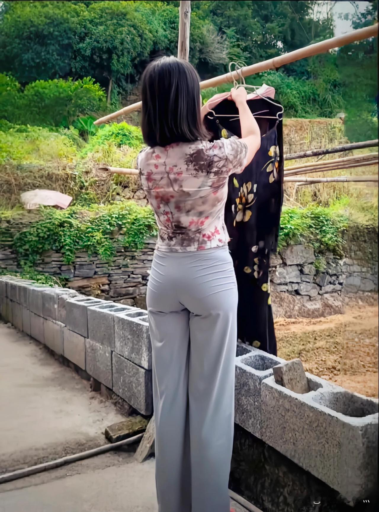 悠游乡间，巧遇晾衣少妇。她手法娴熟地整理衣物，阳光为其勾勒出温柔轮廓。此般寻常画