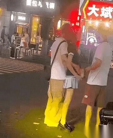 女孩就站在两个男孩中间。
左边那个，手直接揽住她的腰，紧紧贴着。右边那个，当着街