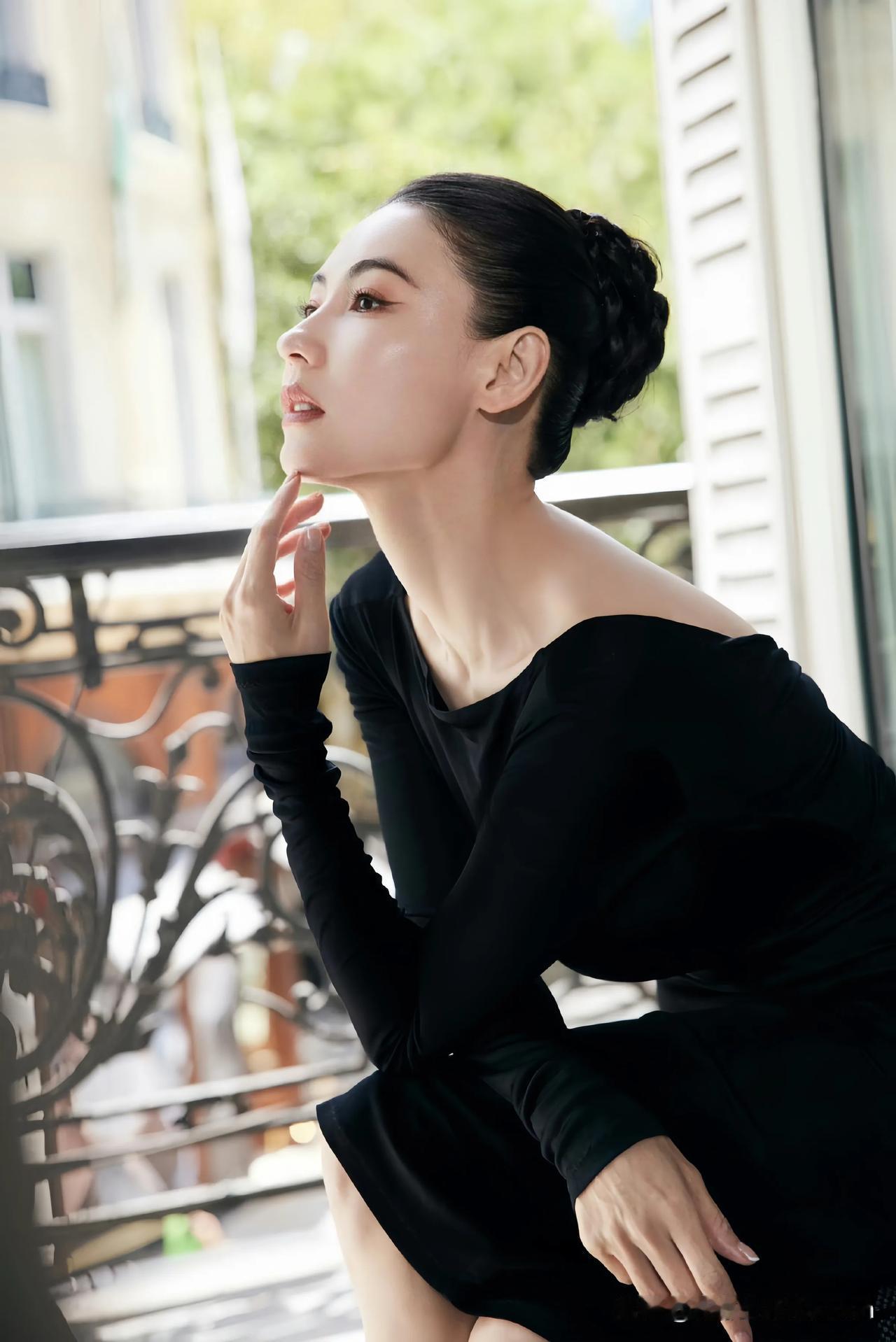 在阳台的光影间，张柏芝尽显优雅魅力。简约的黑色连衣裙勾勒出她曼妙身姿，盘发造型利