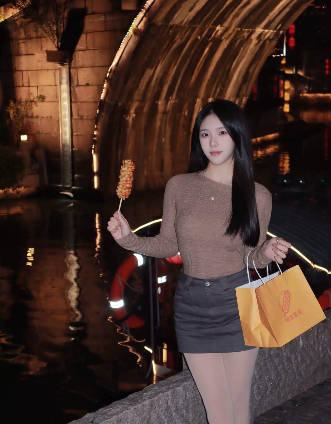 夜晚的街头，甜美少女手拿糖葫芦，漫步在灯光下的桥边。