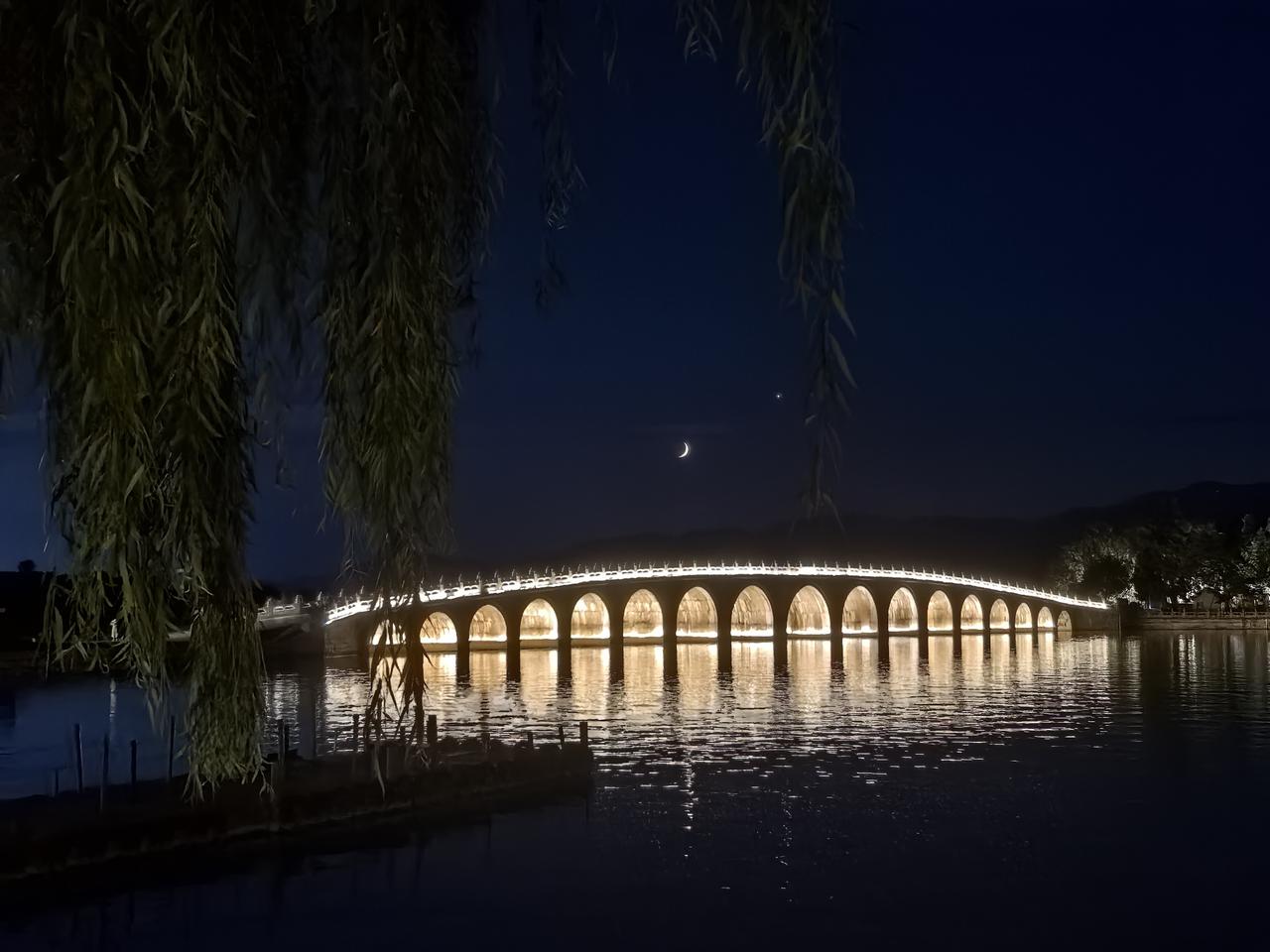 夜色如洗，垂柳如帘，静静半掩着颐和园的万千风韵。

十七孔桥横卧于墨色湖面，暖黄