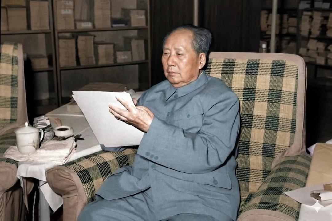 历史老照片，老人家端坐在沙发上，正在聚精会神的阅读一分文件。他衣着朴素，桌子上摆