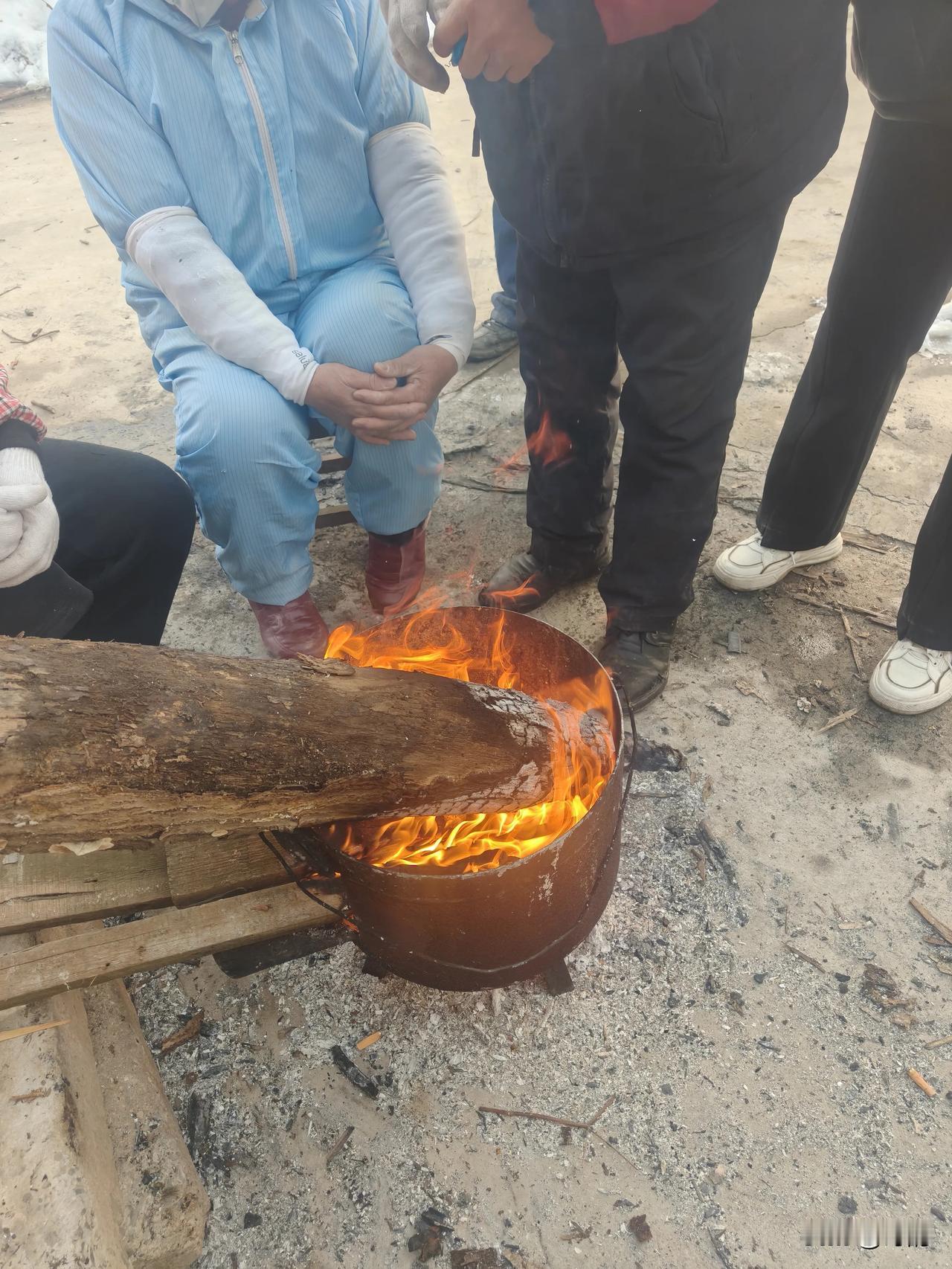 今天在海边的工地旁，撞见了最接地气的取暖方式。一个旧铁桶，一截粗木头，蓝工服的师