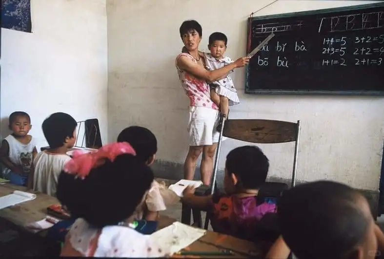 1998年，抱着孩子上课的女老师 1998年，山西省太原市，一间小学教...