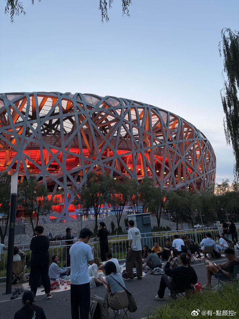 周杰伦鸟巢演唱会外场 场外草坪上坐满了人，看不清舞台但能听清每一首歌，荧光棒在夜