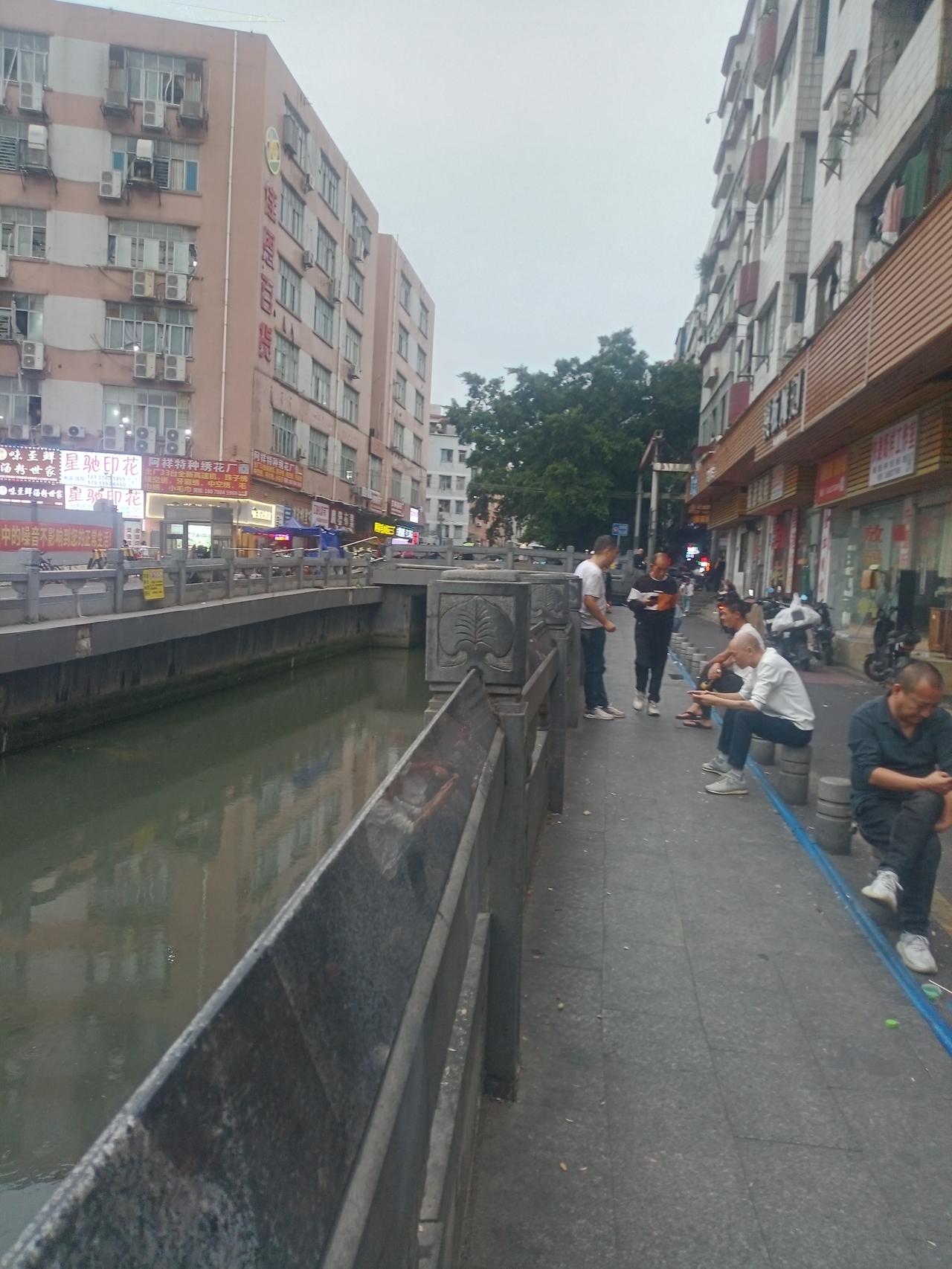 广州康乐村康乐桥河边，好多人做在石凳子上面聊天玩手机。


前面那栋佳恩百货大楼