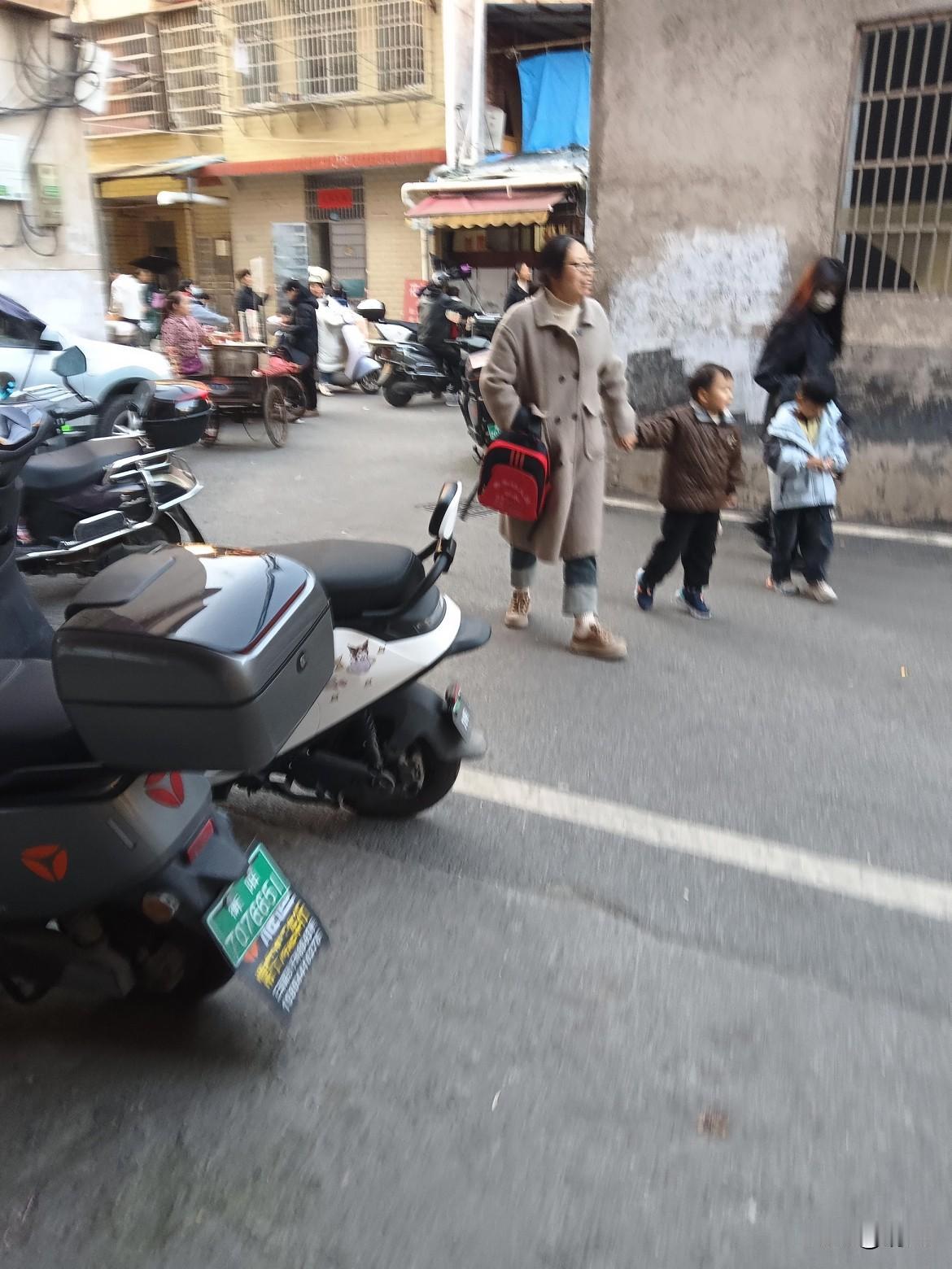 这巷子里的烟火气可太浓了！
你看，阿姨牵着俩娃慢悠悠走着，小家伙们脚不沾地似的蹦