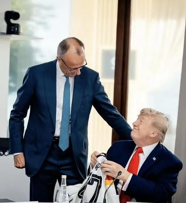 G7峰会现场，默茨捧着印有"TRUMP 47"的德国队球衣走向特朗普，背后三层意