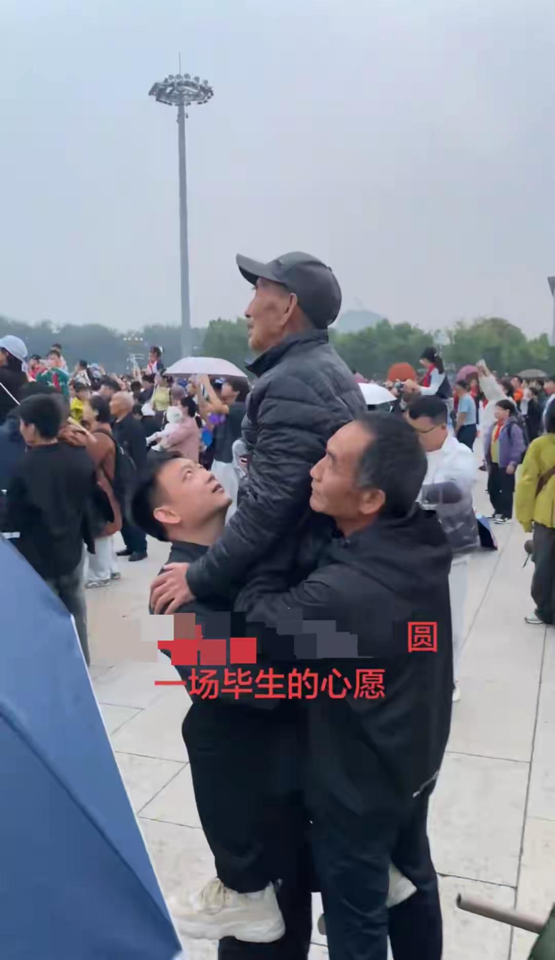 9月29日，天安门广场上，两名男子合力抱住老人，托举他观看升旗仪式。这一幕被网友