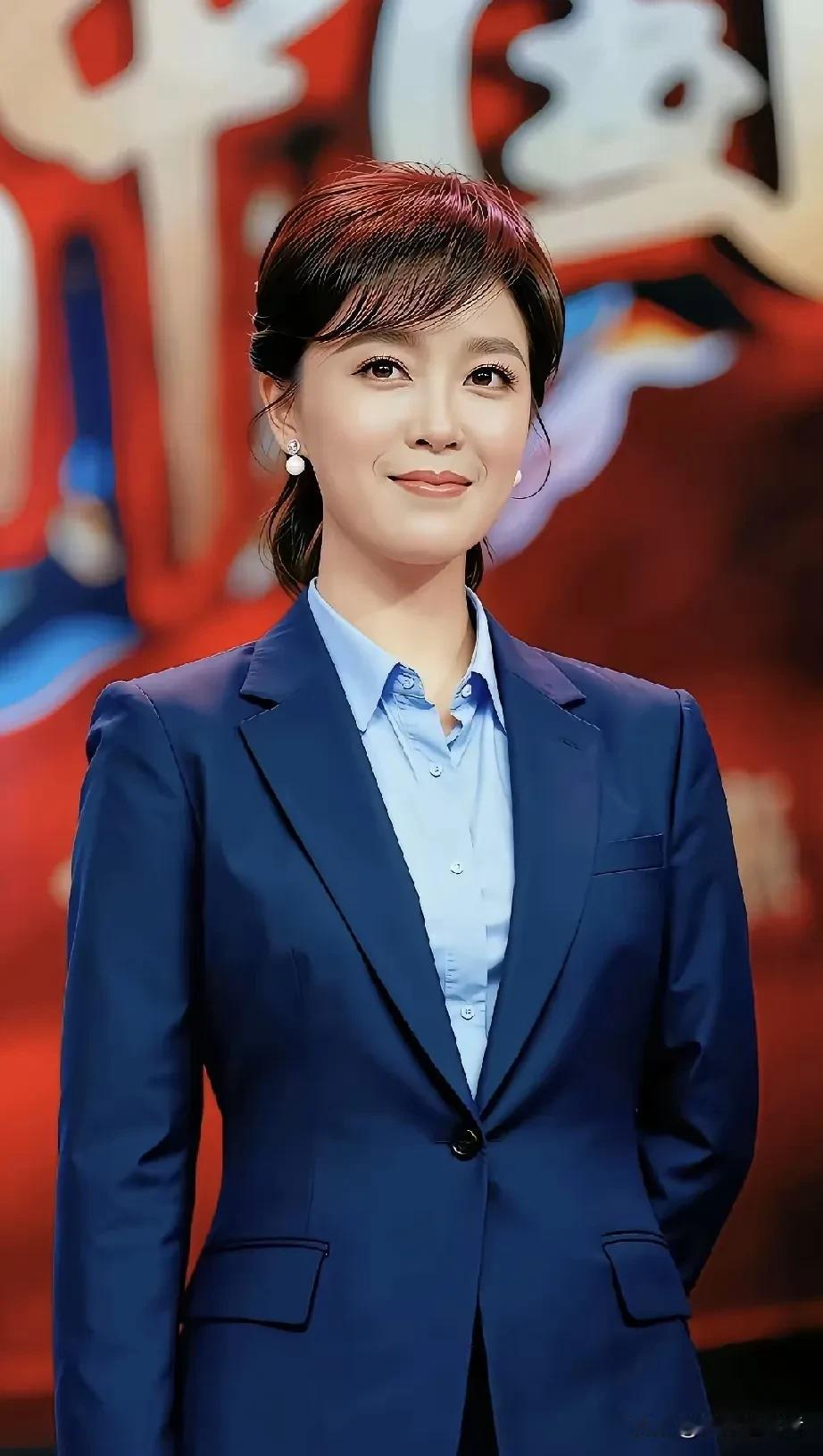 镜头里的她身着一身深蓝色西装套裙，内搭浅蓝衬衫，模样简约利落。珍珠耳饰在发丝间轻