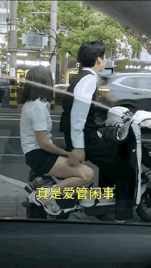 小哥带着女友骑行电瓶车，在路边停车等信号期间对其女友的大腿部进行触碰，让驾驶私家