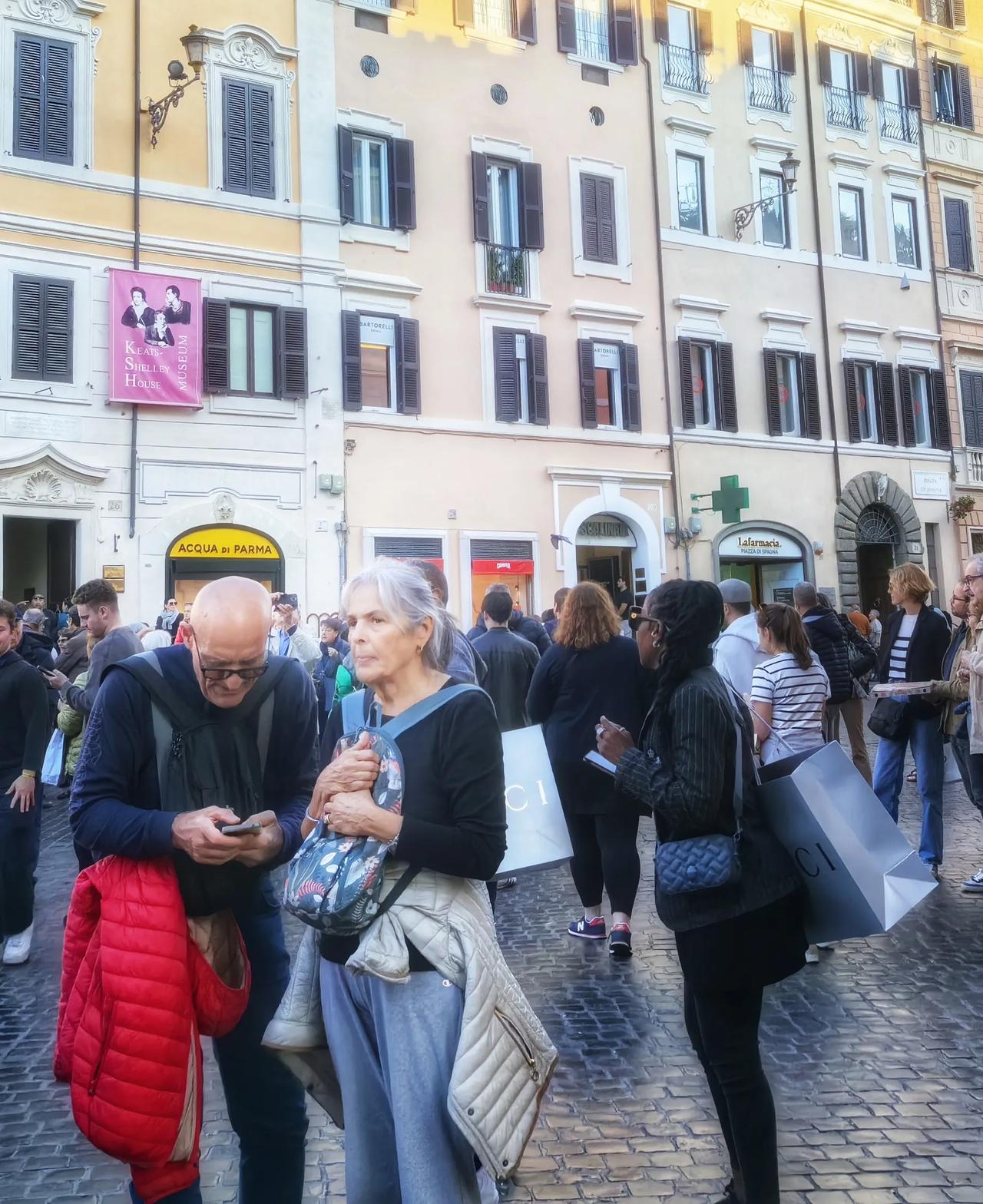 罗马西班牙广场人潮汹涌。一对挎着古驰大礼袋的男女，尤其显眼。古驰男给古驰女女拍照