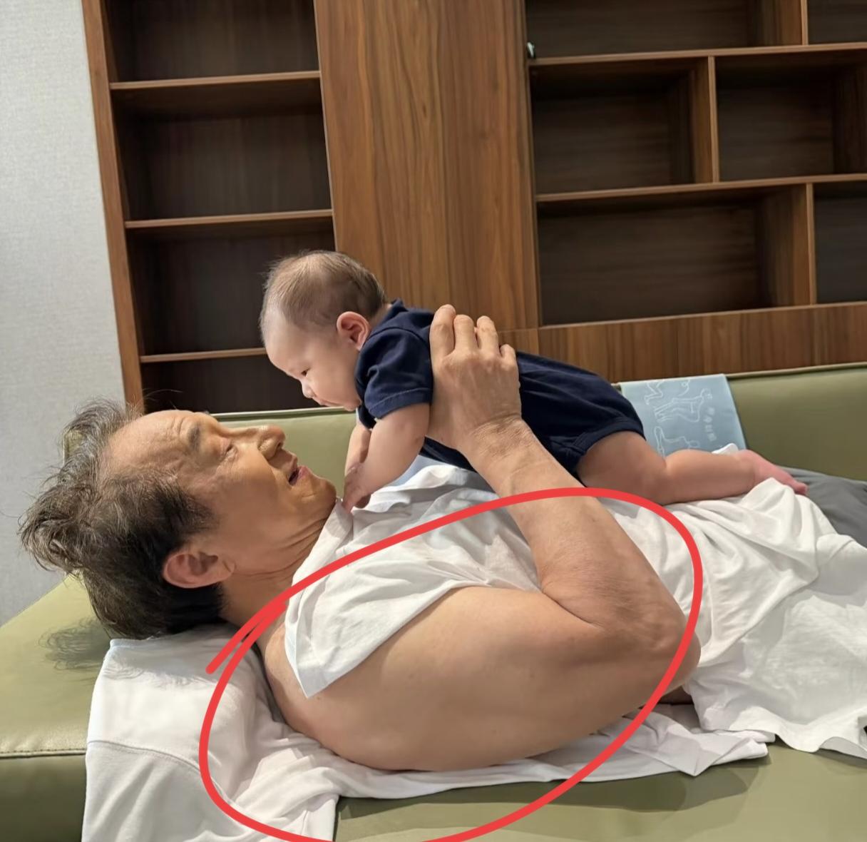 成龙近照曝光！他躺沙发上逗小外甥玩，这大臂是真吸睛，线条紧实饱满，肌肉轮廓格外突