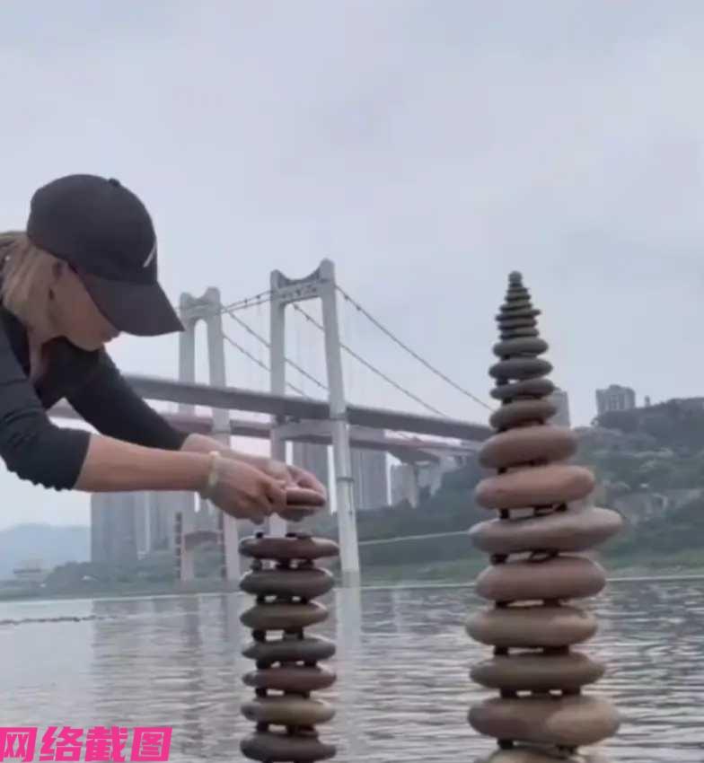 重庆有女子在江边游玩，看到江边有些碎石，不由心动起来，借助石头玩起了垒石头塔，慢