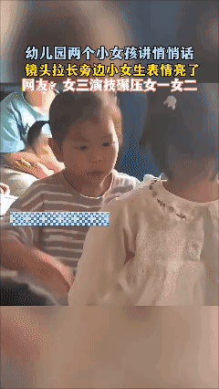 幼儿园两个小女孩讲悄悄话，镜头拉长旁边小女生表情亮了[黑脸]