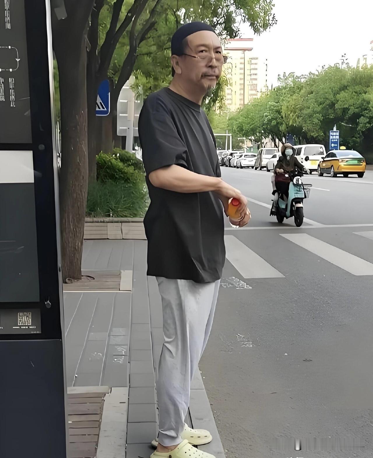 这一位在等公交车的老人，看着很眼熟， 他特别低调，拿着矿泉水，穿着一双拖鞋，安安