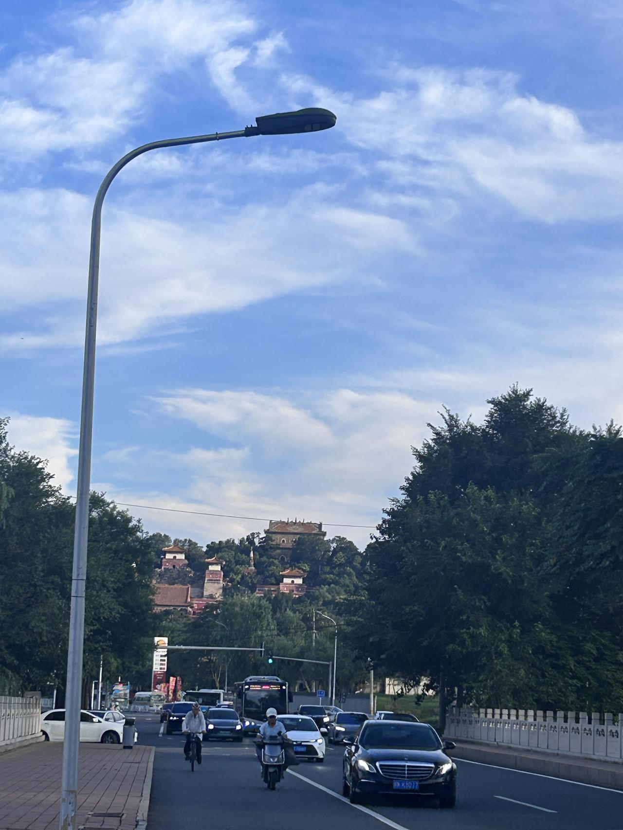 这是白天晴朗天气下北京颐和园附近城市道路的街拍，蓝天铺着舒展的絮状白云，光线明亮