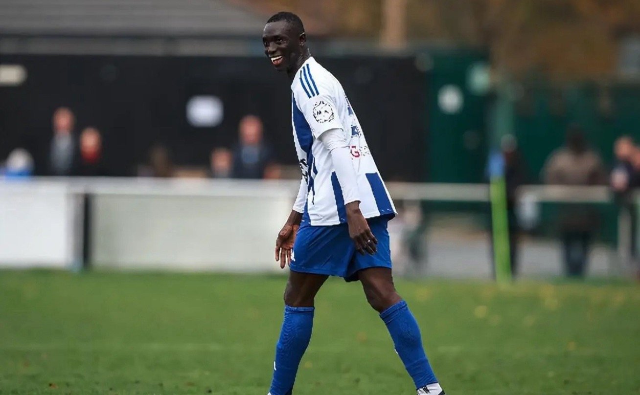 周日下午的曼彻斯特，一座破旧的看台边站着几百个球迷，球场草皮非常不平整，球门后面