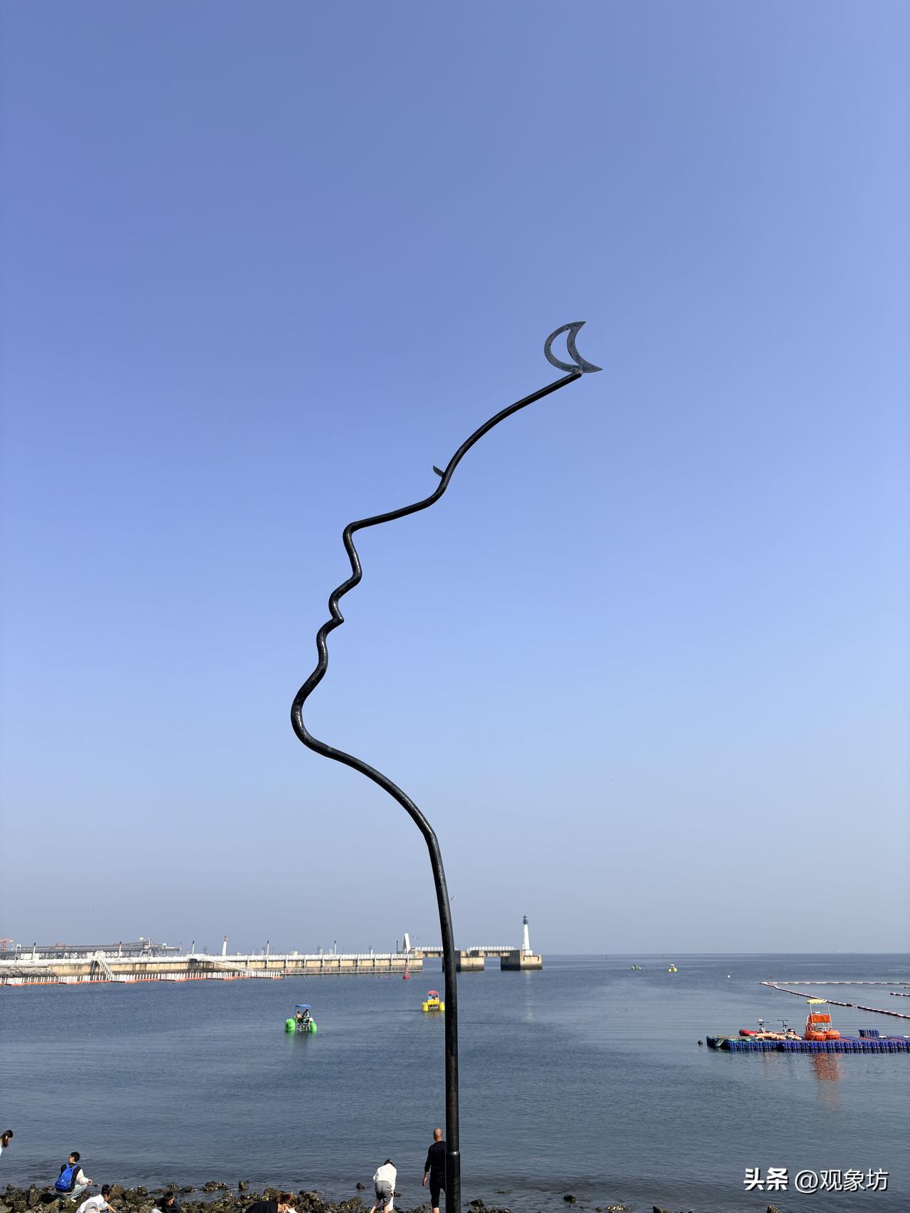 大连梭鱼湾，海风一吹，天蓝得像水洗过一样。海边立着一根黑色的金属雕塑，蜿蜒向上，