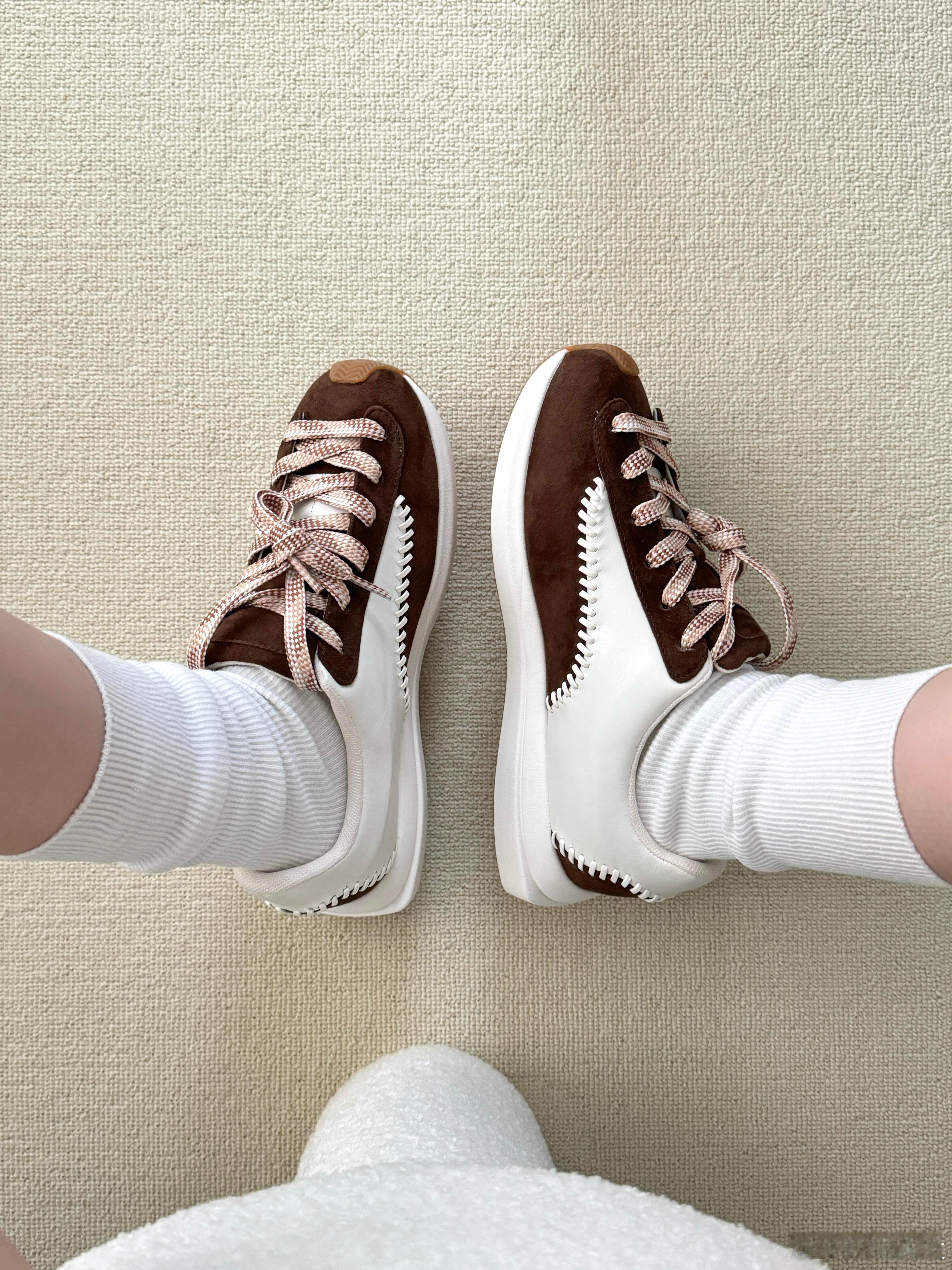 这款运动鞋以独特的拼色设计打造出众的视觉魅力。鞋面主体采用质感高级的棕色麂皮与光