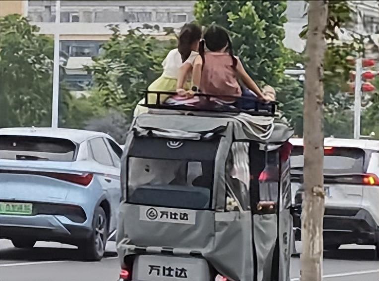 近日，正值下班高峰，路面车流密集。三轮车车顶载两小孩在车流中行驶，无任何防护，当