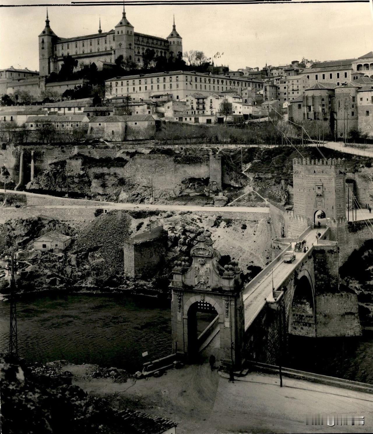 这张黑白照片展示了西班牙托莱多市及其著名的地标阿尔坎塔拉桥（Puente de 