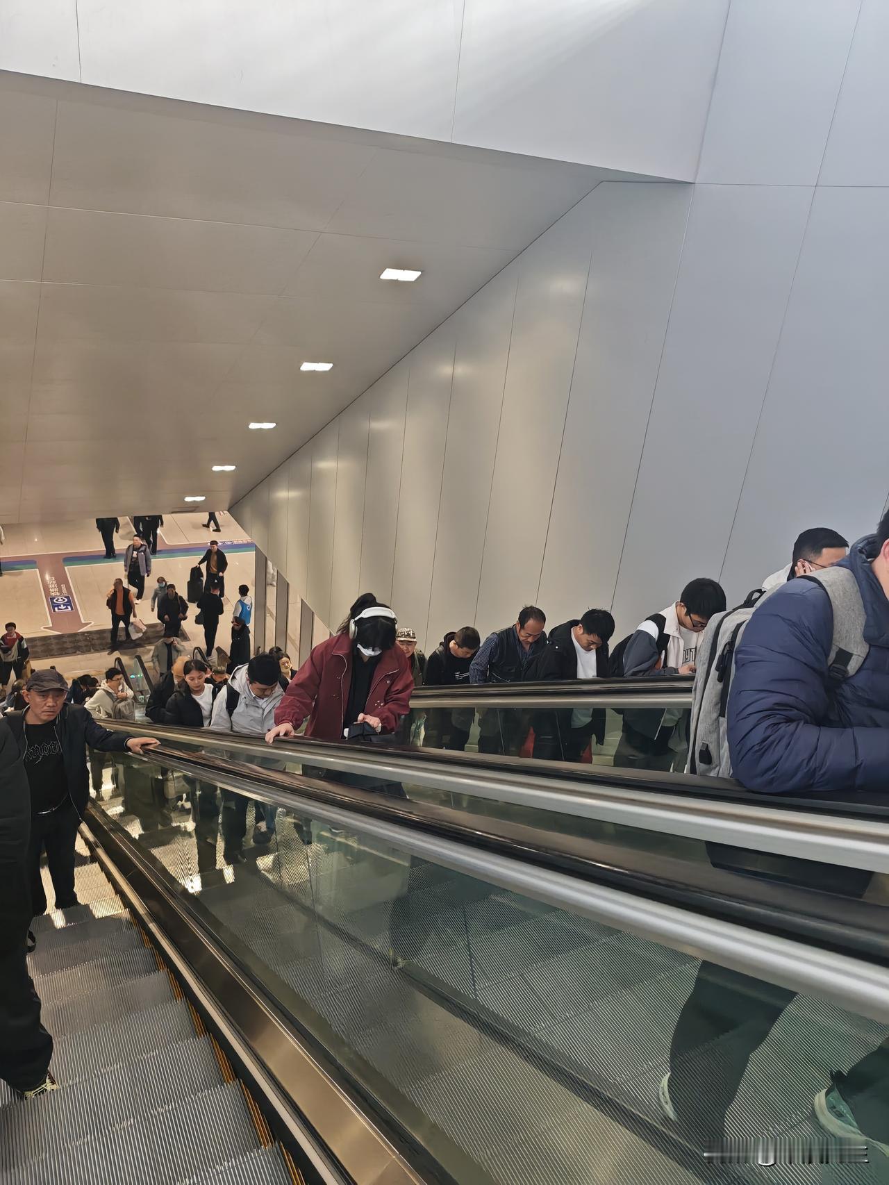 去乘坐火车的人们，站在扶梯上，低头看手机，由着扶梯一点点往上走。到了安检入口，人