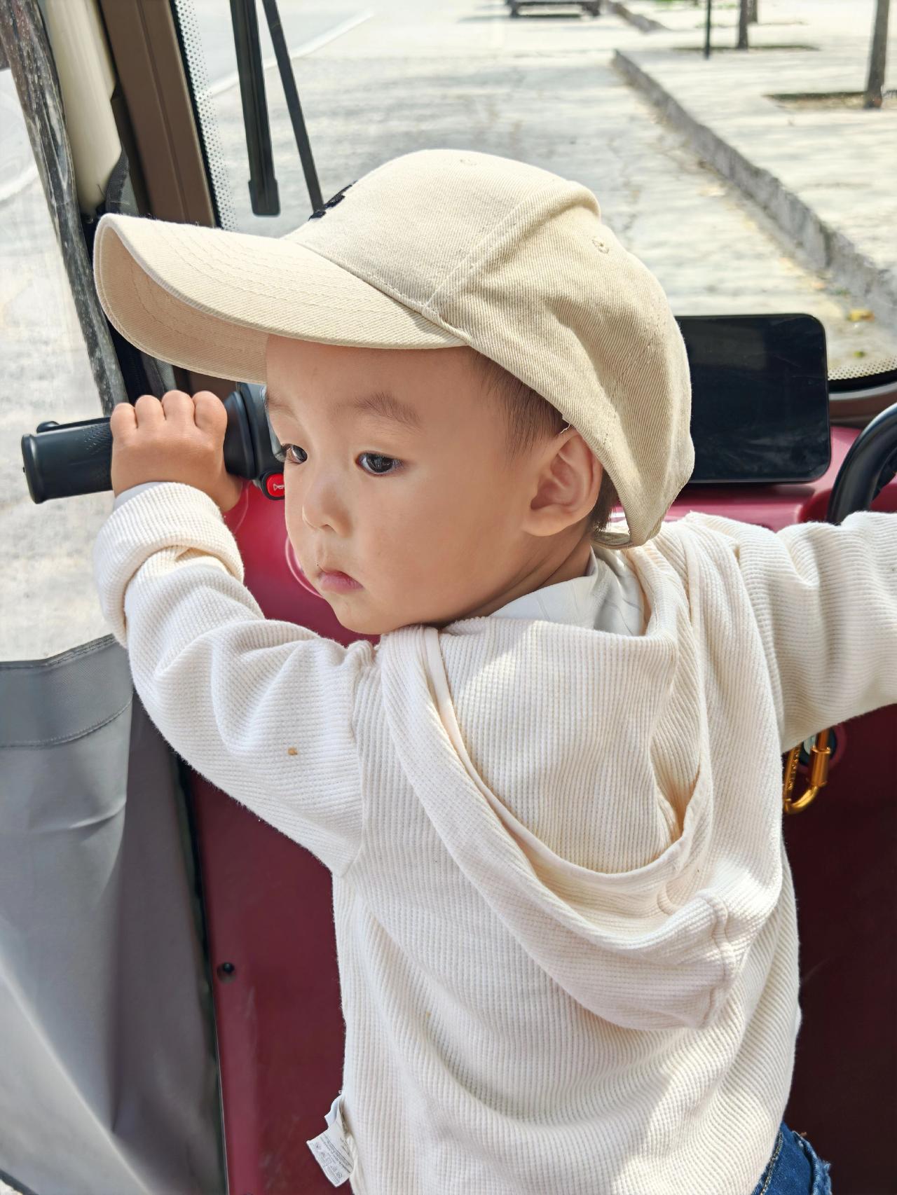 阳光洒在车窗上，小宝贝扶着栏杆，仿佛在探索世界的边界。帽子下的小脸蛋透着好奇与纯