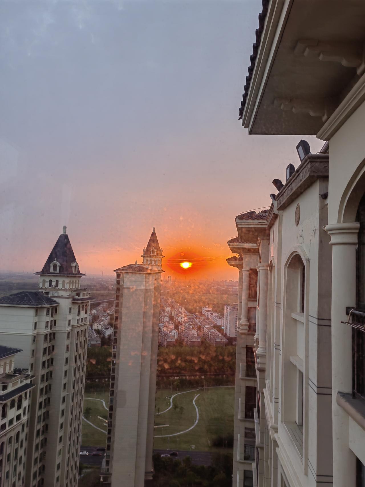 夕阳西下
站在窗边，看落日把天空揉成橘子汽水色。
欧式尖顶的楼宇，被镀上一层暖融