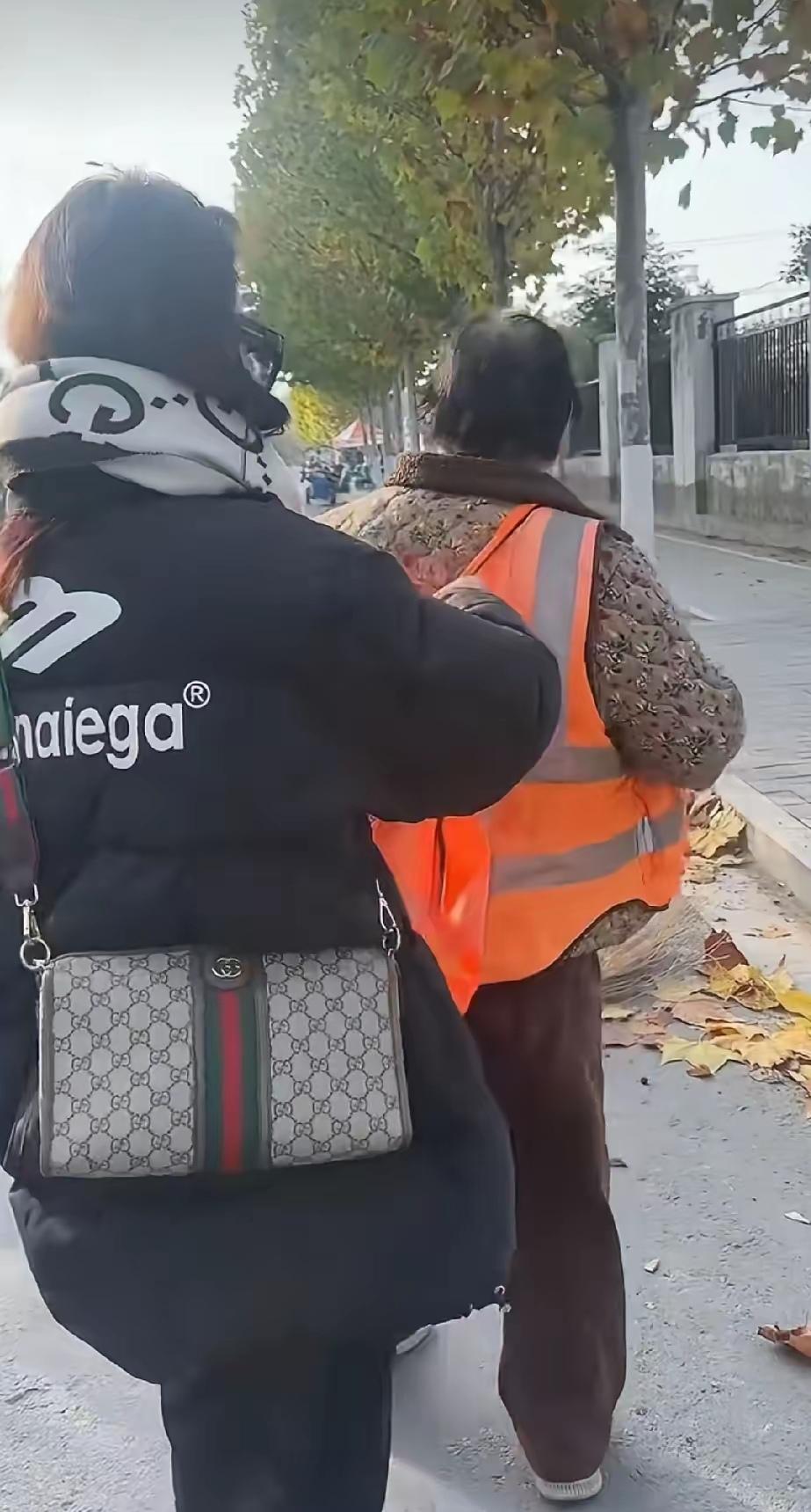 环卫工阿姨正在清扫地上的落叶，
一名年轻女子突然走过去脱掉了阿姨身上的工作服，接