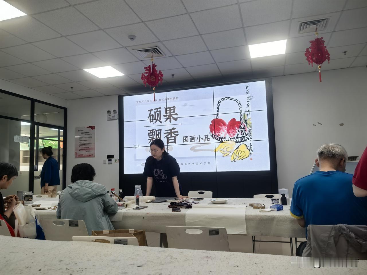 首都师范大学美术学院的学生指导社区国画班的学员学画。