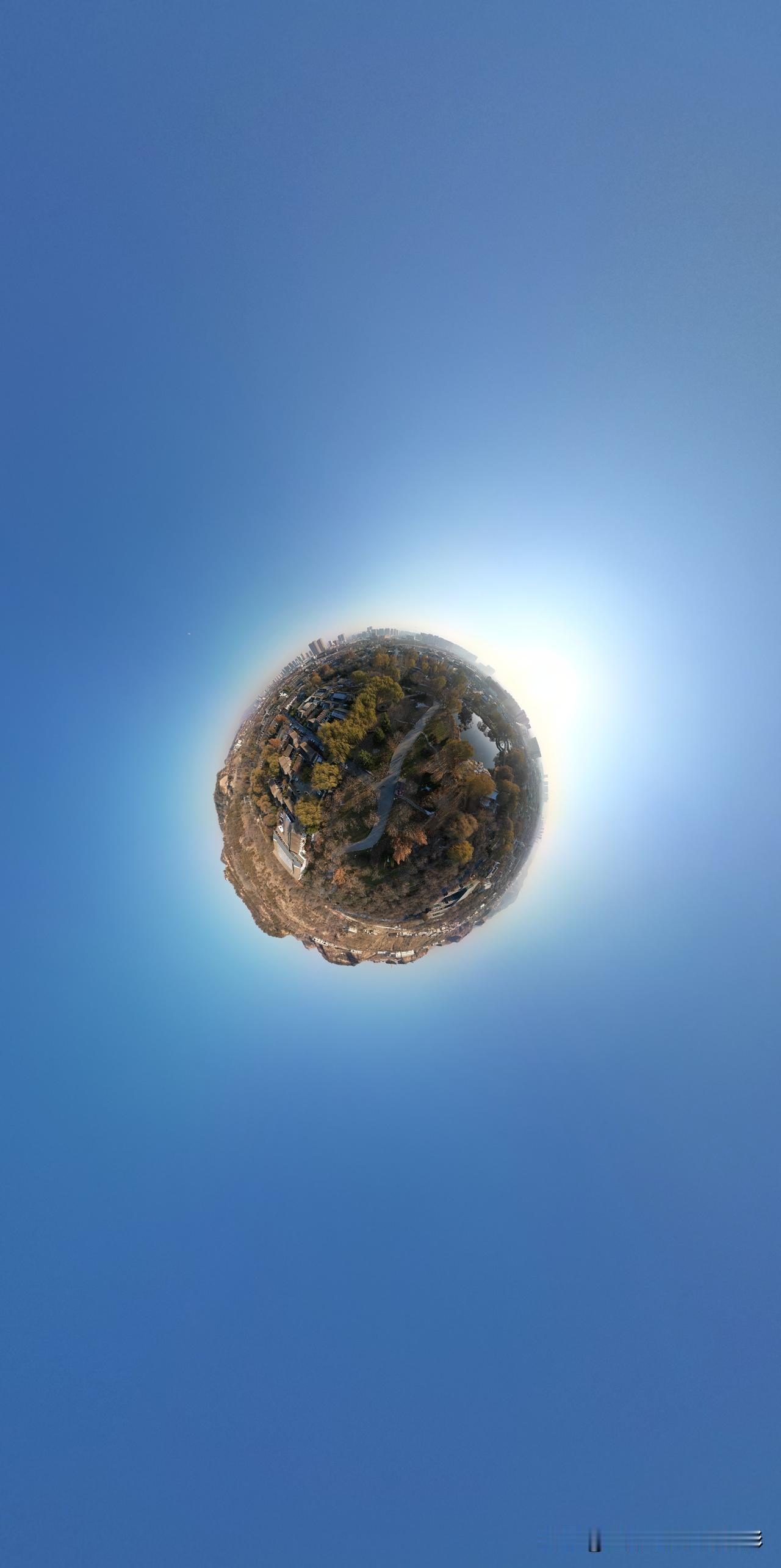 仁寿山小星球全景图中，天空湛蓝如洗，星球边缘树木与建筑错落分布，阳光洒下形成淡淡