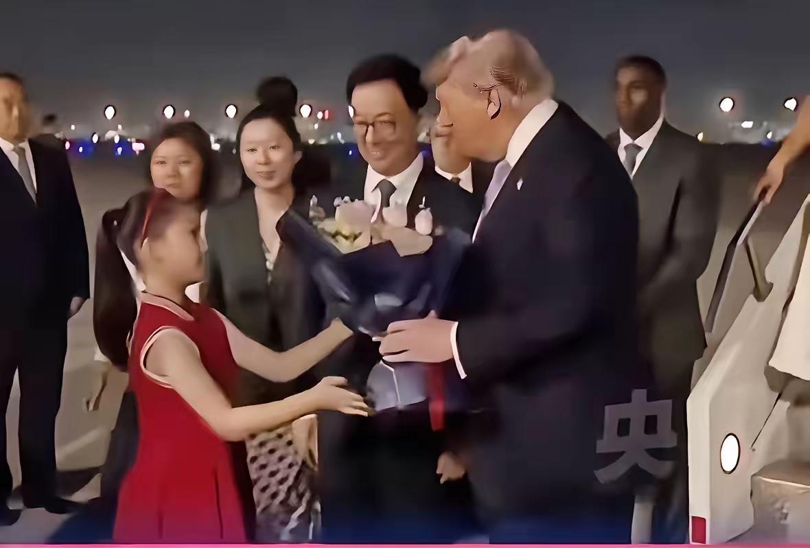 特朗普来了，观影人群都是穿着深色服装，只有这个穿红色连衣裙的小姑娘，手捧鲜花，送