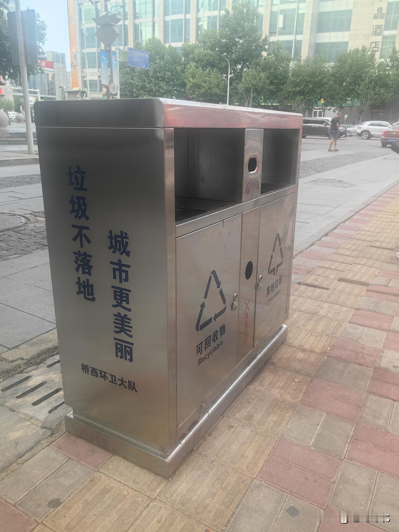 “垃圾不落地，城市更美丽”标语醒目，但环卫设施摆放忽视盲道通行需求。对于依靠盲道