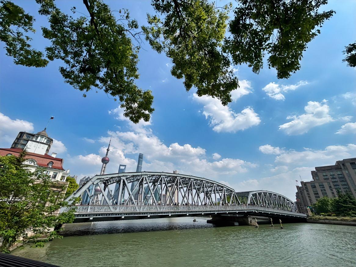 外白渡桥畔的绿茵遮荫和上空的蓝天白云，互为映衬，在熙熙攘攘的人流面前，有此一处岁