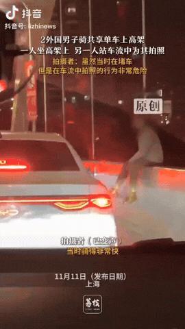 11月11日，上海，2外国人骑共享单车上高架，一人坐在高架上，另一人在车流上为其