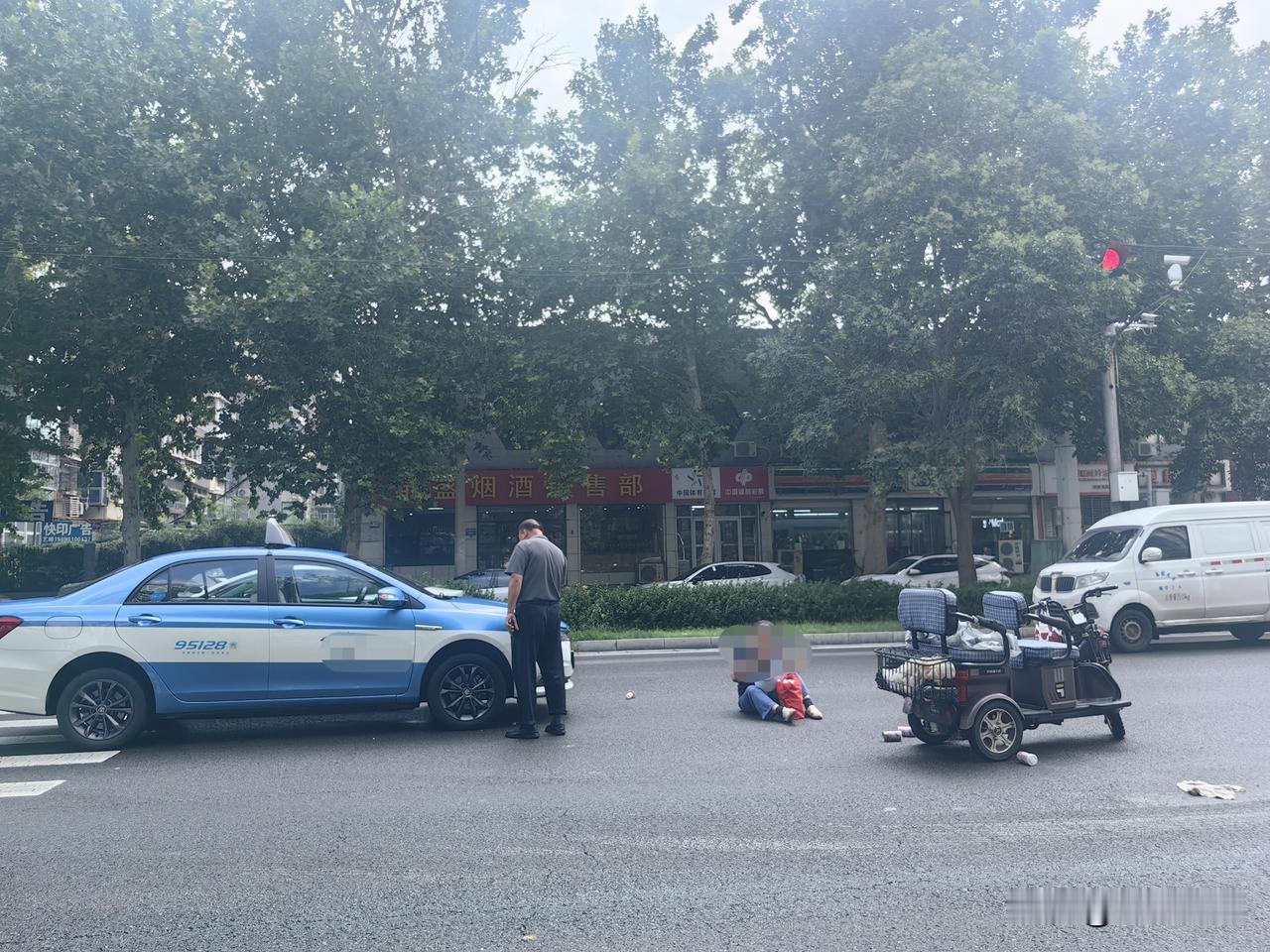 现场可以看到，电动三轮车停在路面，驾乘人员坐在道路上，出租车停靠一旁，双方人员在