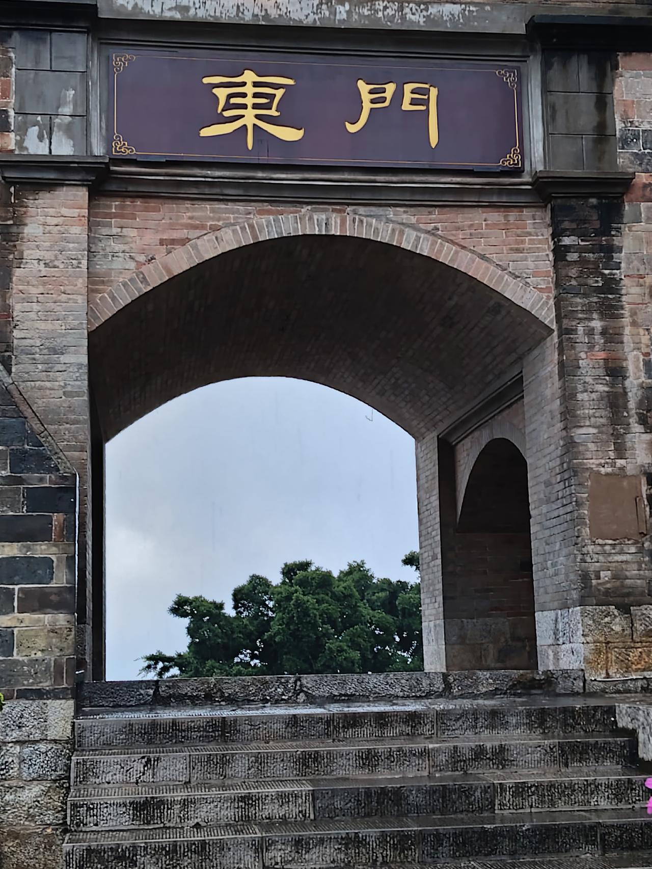 红河老城的东门城楼，檐角下悬着一方楠木老匾，木色已深褐近黑，唯独“东门”二字以金