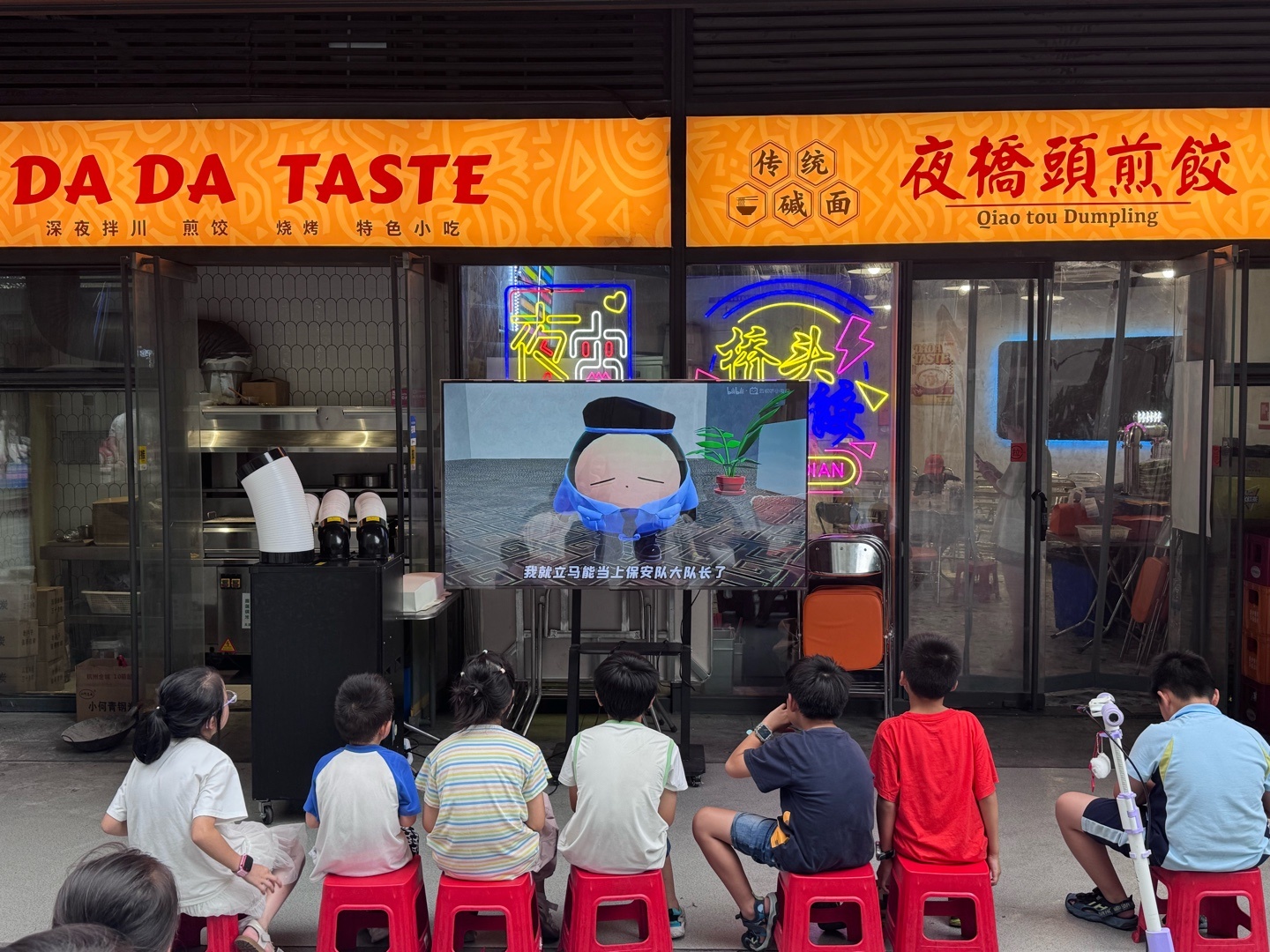 一群小朋友在餐厅前排排坐，在看B站的似乎是蛋仔派对的视频，氛围真好啊！ 