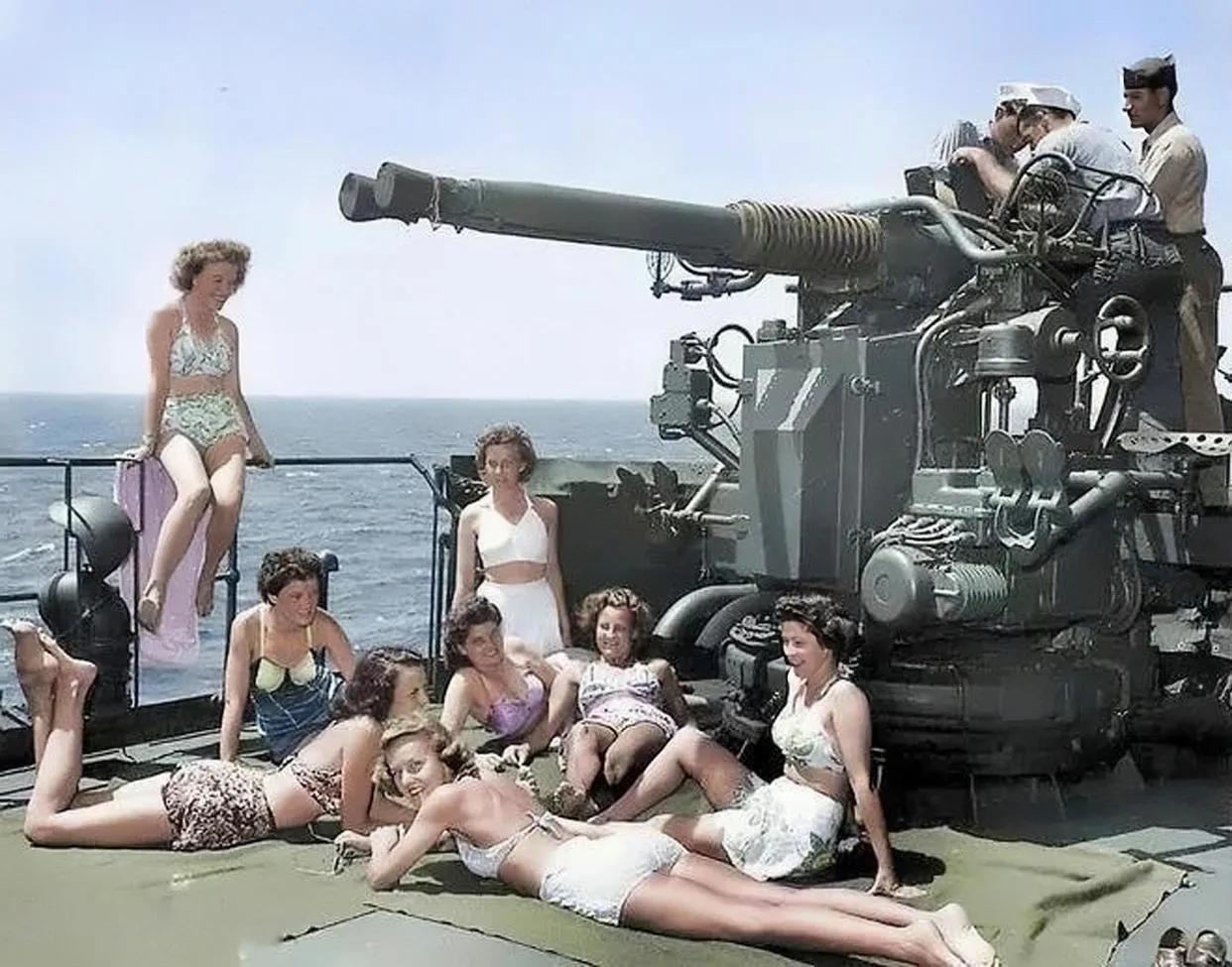 这美军真会玩，女兵穿着比基尼在甲板上晒阳光浴，一旁的男兵在修理武器。

下图是二