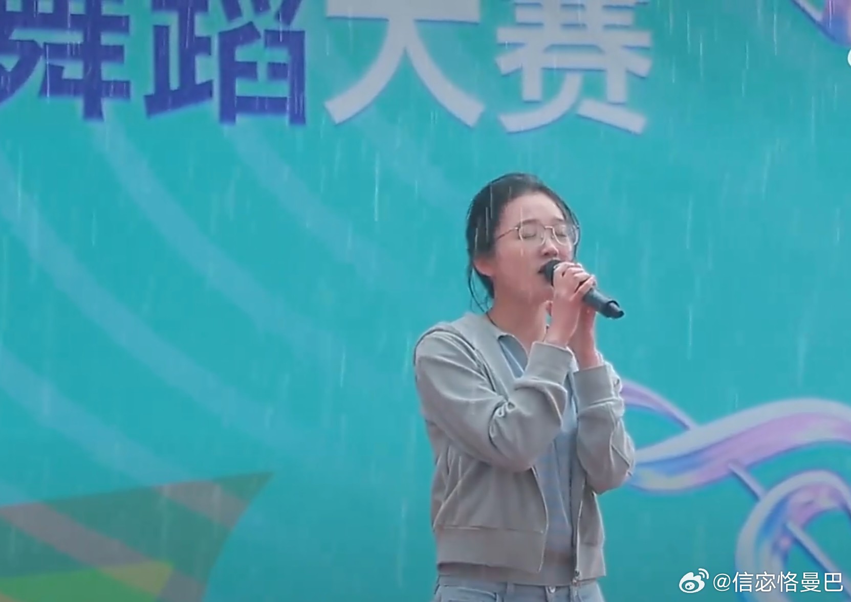 雨幕漫过舞台檐，她执麦轻吟，声线绕着雨丝漫；他举伞立身旁，蓝衫身影，为她撑起晴光