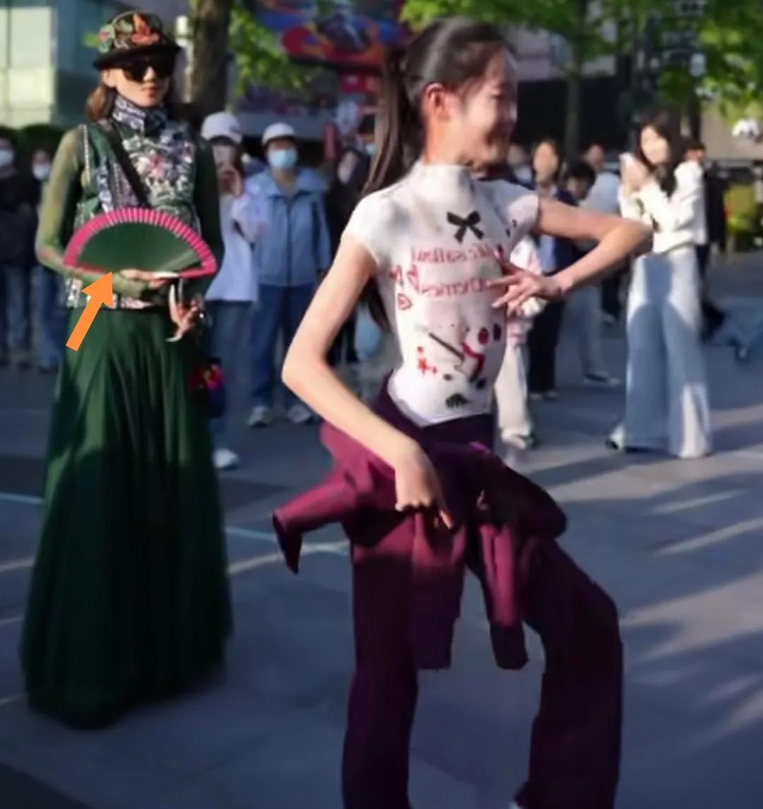 杭州西湖边杨丽萍手拿折扇欣赏一女生独舞。