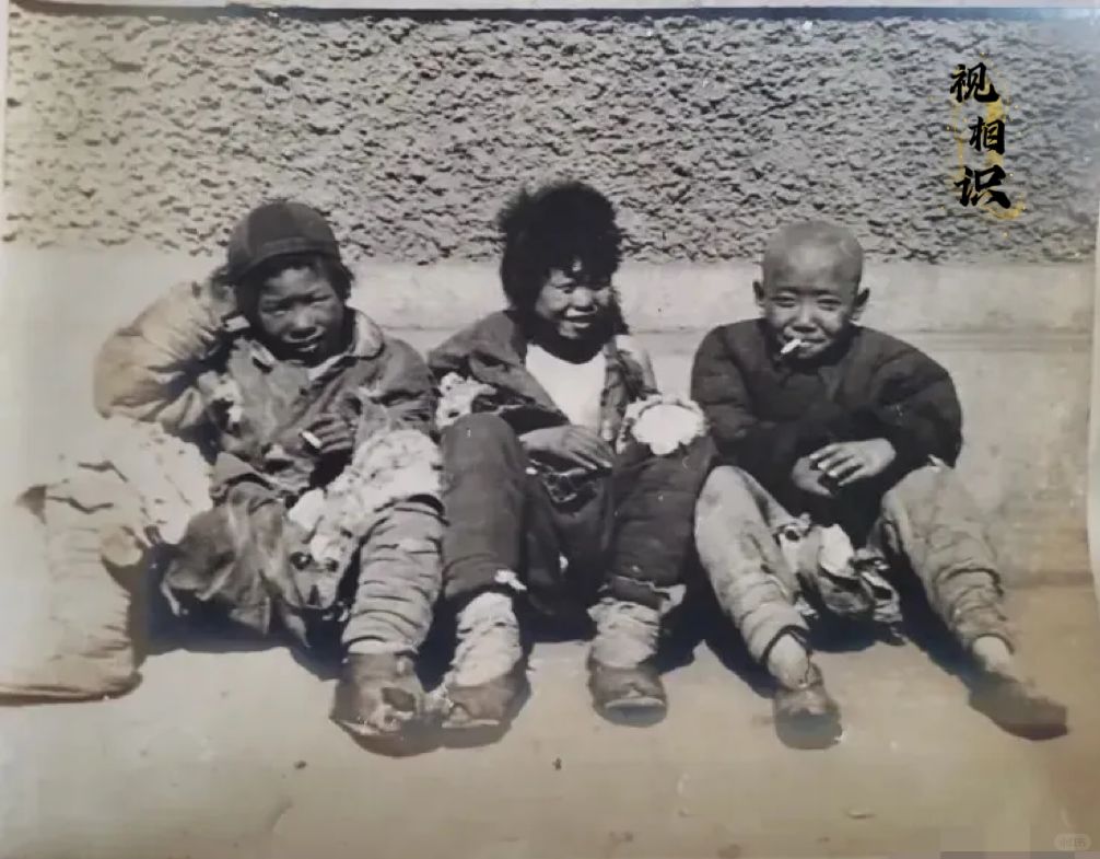 1936年，北平街头，三名乞丐坐在墙角晒太阳的老照片，镜头中他们都衣衫褴褛，浑身...