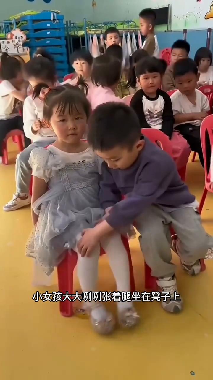 懂事的小暖男。
一看幼儿园里这一幕真的太暖心了。小女孩大大咧咧张着腿坐在凳子上，
